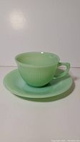 Photo of jadeite green Fire King teacup on matching saucer, showing overall shape, color and finish.