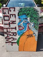 Front side of the wooden board painting featuring Joker with green hair and blue facial paint, text to the left 'LET FRAME GO FLAW'.