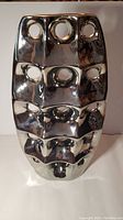 Front view of metallic ceramic vase showing three vertical rows of circular hollow cut-outs and the reflective finish.