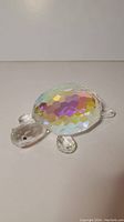 Cut crystal turtle figurine showing iridescent, faceted shell and transparent faceted feet and head, photographed on white background.