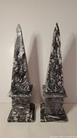 Full front view of two marble obelisks side by side showing the overall shape, height, and marbled pattern.