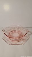 Pink depression glass bowl with handles nested in matching eight-sided plate with rim