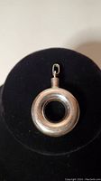 Front view of circular sterling silver perfume pendant showing hollow center and metal loop for chain attachment.