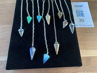 Top down view of 10 gemstone pendulums arranged on black cloth with visible chains and pointed stone pendants.