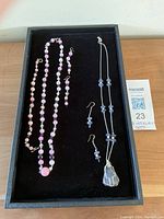 Two handcrafted jewellery sets on black velvet tray: pink morganite bead necklace and earrings on the left, black agate pendant necklace and earrings on the right.