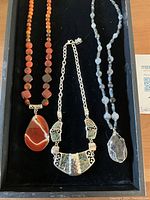 Close-up of necklaces showing orange agate necklace with large pendant, abalone necklace, and labradorite necklace