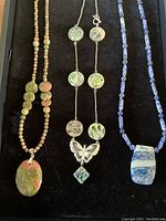 Top-down view of the three necklaces on a black velvet tray showing all the detailed beads and pendants.