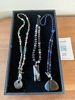 Full view of three gemstone bead necklaces laid in a tray showing details of beads and pendants.