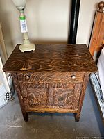 Full view of the antique tiger oak washstand showing the original wood finish, drawer, and cupboard door with wooden knobs.