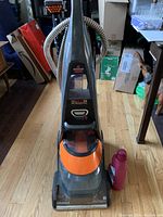 Full view of upright carpet shampooer with hose attachments and cleaning solution bottle