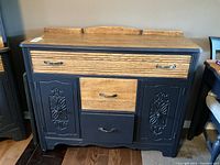 Front view of buffet showing natural wood top and drawer fronts paired with dark blue painted body and decorative door panels.