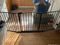 Full view of the black metal baby gate spanning across a kitchen floor area, showing the vertical bars and overall size.