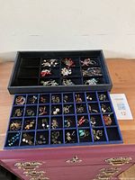 Two trays filled with assorted handcrafted gemstone earrings with sterling silver ear wires, arranged individually in compartments.