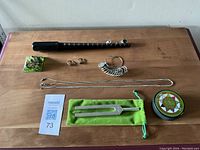 Full lot overview on wooden surface, showing ring sizer, rings, chains, tuning fork, and container