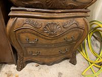 Front view of one wooden nightstand showing curved drawers with metal handles and shell carving
