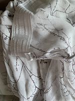 Close-up of the curtain fabric showing the dark branch pattern on white sheer material and pleated header with hooks.