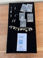 Full view of all jewelry items on black display including pendants, sealed bags of earrings, and charm bracelet laid out.