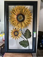 Full view of the metal sunflower wall hanging inside a black frame showing two large sunflowers and green leaves.