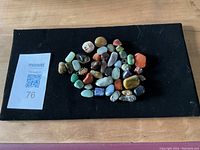 Top view of 32 assorted tumbled stones on black fabric, showing variety in color and size.