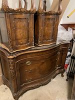 Large wooden dresser with curved front, carved details, glass top, and brass handles.