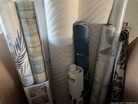 Wallpaper rolls showcasing different patterns and textures arranged upright against a wall.