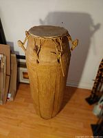 Full view of the large standing African drum showing height, wooden body, and rope-tied drumhead