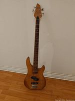 Front view of the full bass guitar showing natural wood finish, headstock, neck, fingerboard, pickups, control knobs, bridge, and strings.