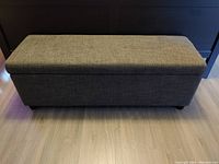 Front view of rectangular gray fabric-covered blanket chest bench closed.