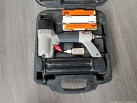 Open carrying case containing a gray and black Porter Cable brad nailer with red trigger and two boxes of Paslode brad nails above it.