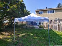 Fully assembled 10-foot white pop-up canopy set up outdoors in a backyard.