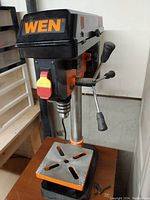 Front view of WEN drill press showing spindle, three-handle control lever, and base with adjustable table.