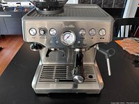 Front view of stainless steel espresso machine showing control buttons, grind amount dial, filter size selector and analog pressure gauge.