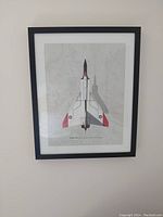 Photo of framed print on wall showing overhead view of Avro Arrow aircraft with black frame and white mat.