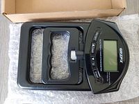 Digital grip strength tester device shown outside packaging on bubble wrap, displaying LCD screen and adjustment knob.