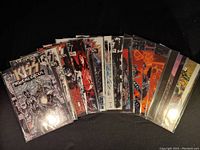 Photo of first batch of KISS Psycho Circus comics showing covers with band members in theatrical costumes and stylized artwork, comics in protective plastic sleeves.