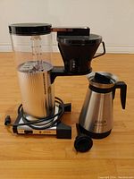 Front view of coffee maker showing water reservoir, filter basket, and thermal carafe