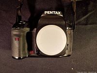 Front view of Pentax K10D camera body with body cap attached and strap