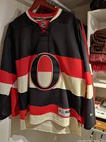 Front view of the black Ottawa Senators third jersey with red and white horizontal stripes and large 'O' logo