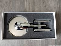 Stainless steel pizza cutter shaped like U.S.S. Enterprise resting in foam packaging