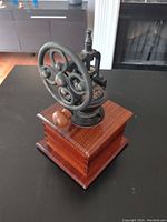 Side angle view of vintage coffee grinder showing wooden base and large cast iron grinding wheel.