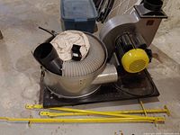 Workshop dust collector unit on black base with yellow motor cover, flexible hose, and fabric filter bag visible.