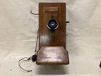 Front view of antique wooden wall phone with black earpiece, buttons, and crank.