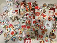 Wide shot showing numerous antique valentines of various designs including heart shapes, characters, animals and flowers spread out on a flat surface.
