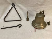 Large brass bell, metal mounting arm, a metal mounting bracket, dinner triangle and a metal striker displayed on a cloth surface.