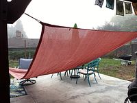 Photo showing the orange triangular shade sail installed over a patio with outdoor furniture beneath.
