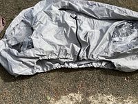 Light gray bike cover with visible elastic edges and center tuck strap, spread on ground