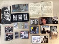 Photo showing a collection of Bob Dylan CDs, cassette tapes, booklet, and a songbook including The Bootleg Series box set, Live 1964, and others.