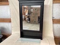 Full front view of black Hemnes wall cabinet with mirror, standing upright on a cloth backdrop.