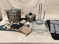 Overall view of lot contents including cookware, mitts, glass dish, paper towel holder, placemats, spoon rest, funnel, and silverware holder.