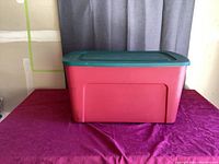 Red rectangular plastic container with green lid placed on purple surface, shown from the front.